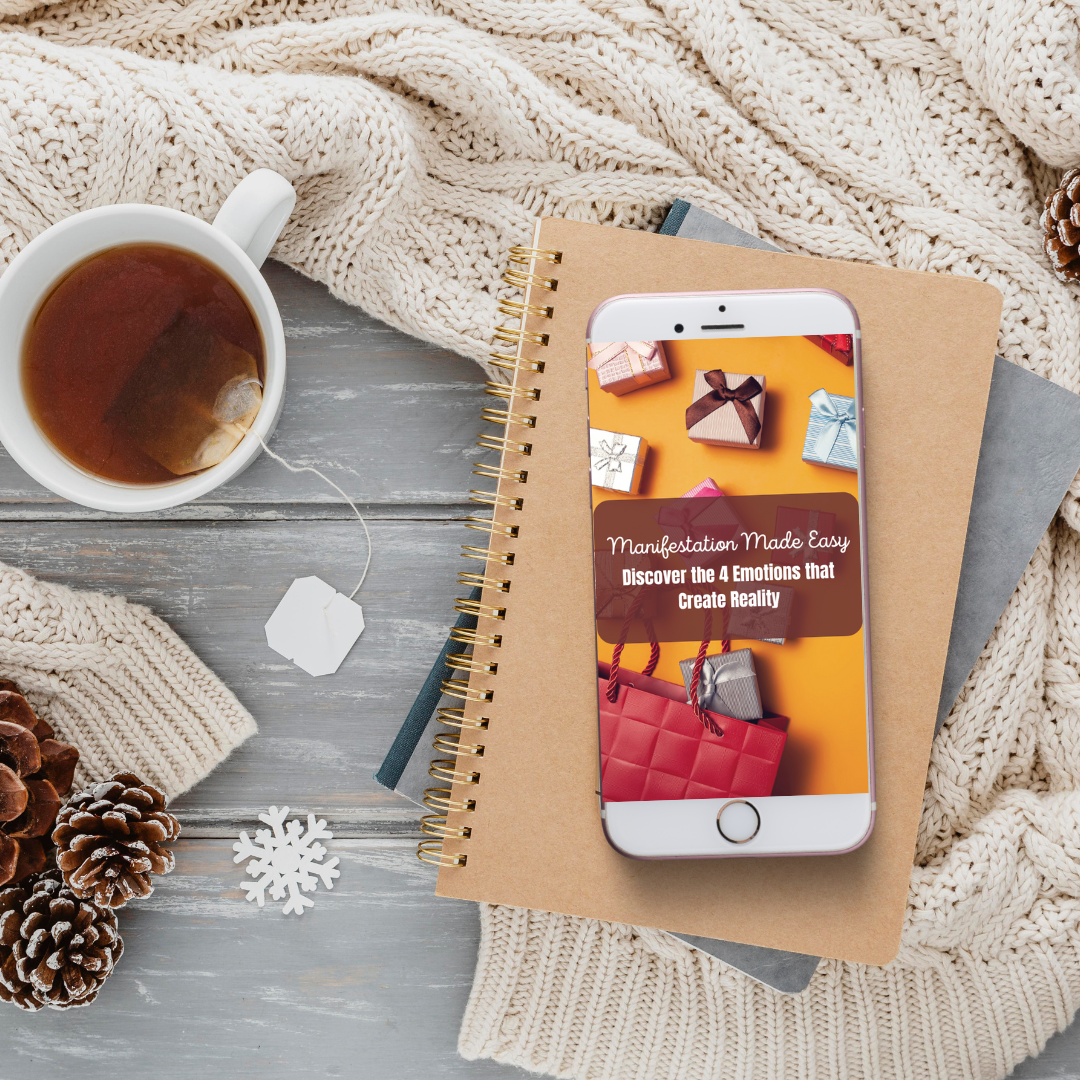 Phone displaying a book cover on a notebook with a cup of tea and decorative items on a textured surface that features a digital guide titled " manifestation made easy "
