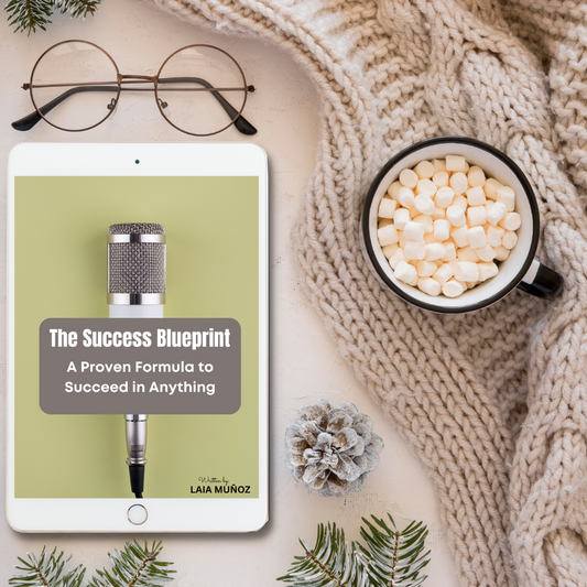 An image featuring a tablet displaying the cover of the book 'The Success Blueprint. A Proven Formula to Succeed in Anything', accompanied by a microphone, glasses, a cup of hot chocolate with marshmallows, and a cozy knit blanket and you can buy it at ww.laiamunozauthor.com